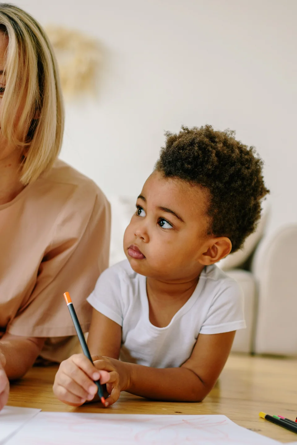 Anak kecil duduk di meja kayu sambil belajar memegang pensil dan menggambar