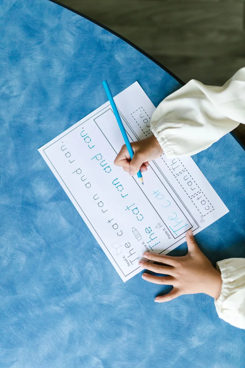 Tangan anak menulis dan melacak huruf di worksheet calistung printable modul Sensim